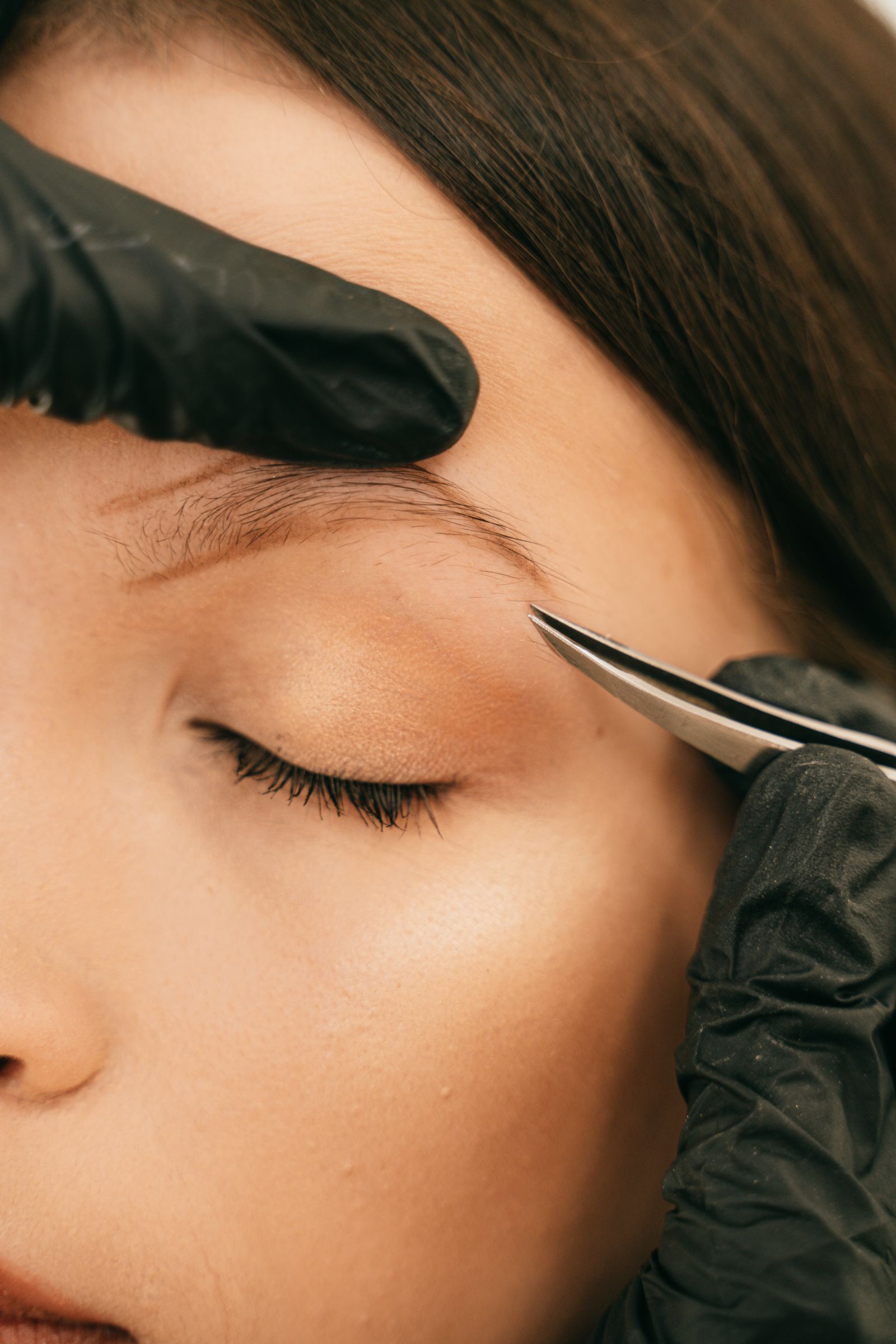 Beauty professional shaping a client’s eyebrow with tweezers